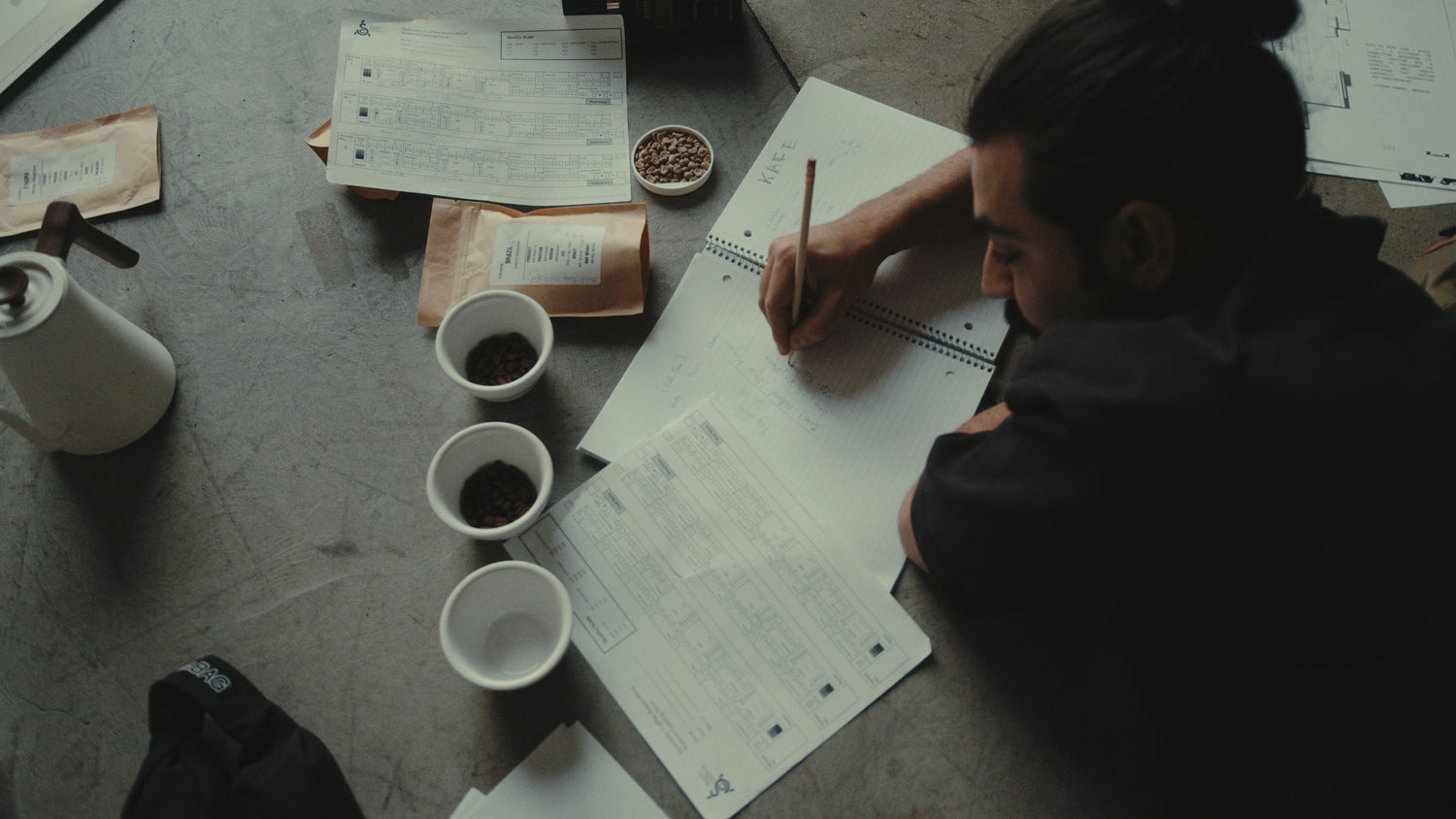 Person sitting at a table with KAFE coffee beans and paper
