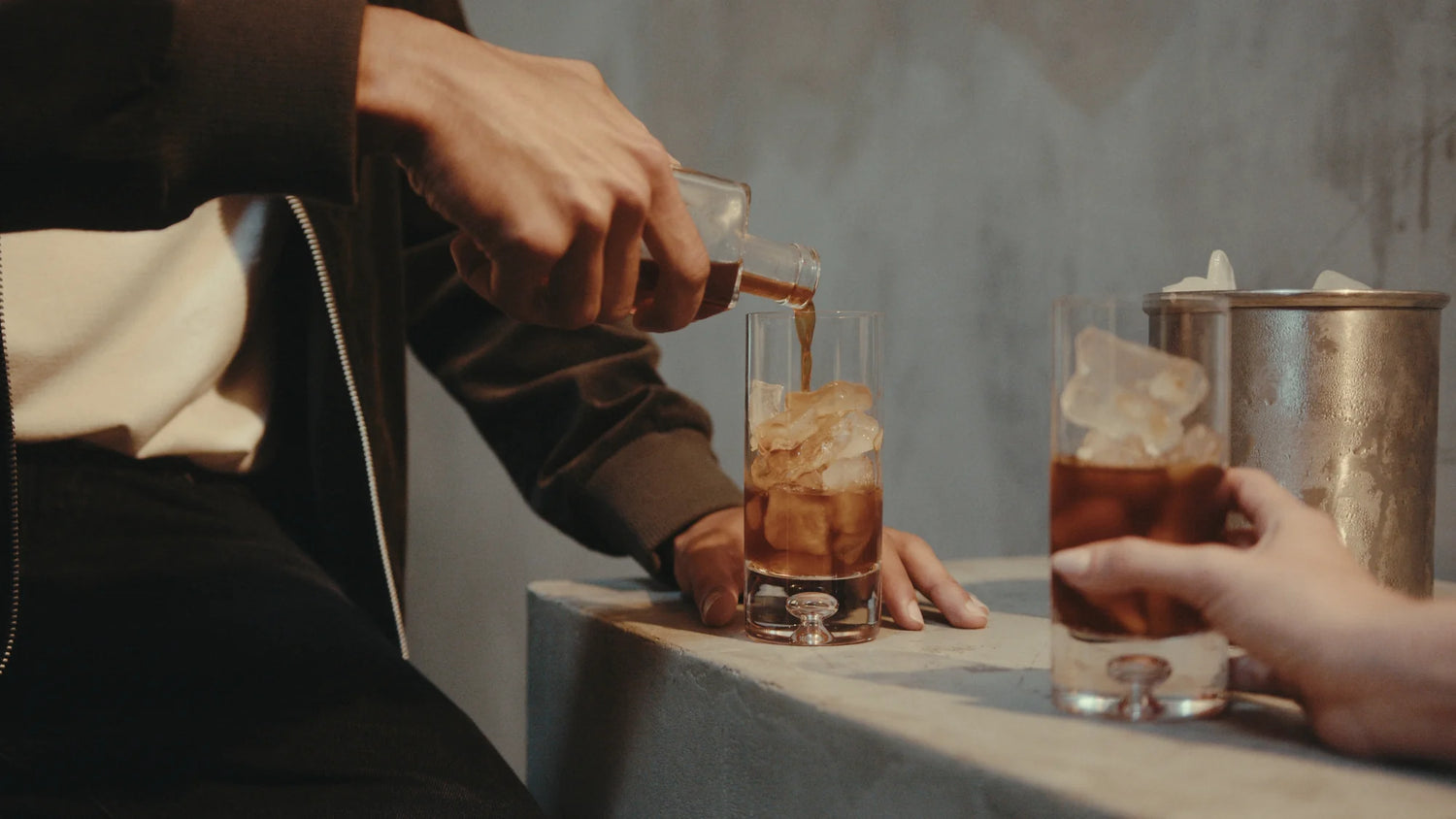 Person pouring a KAFE coffee into a glass with ice on a table.