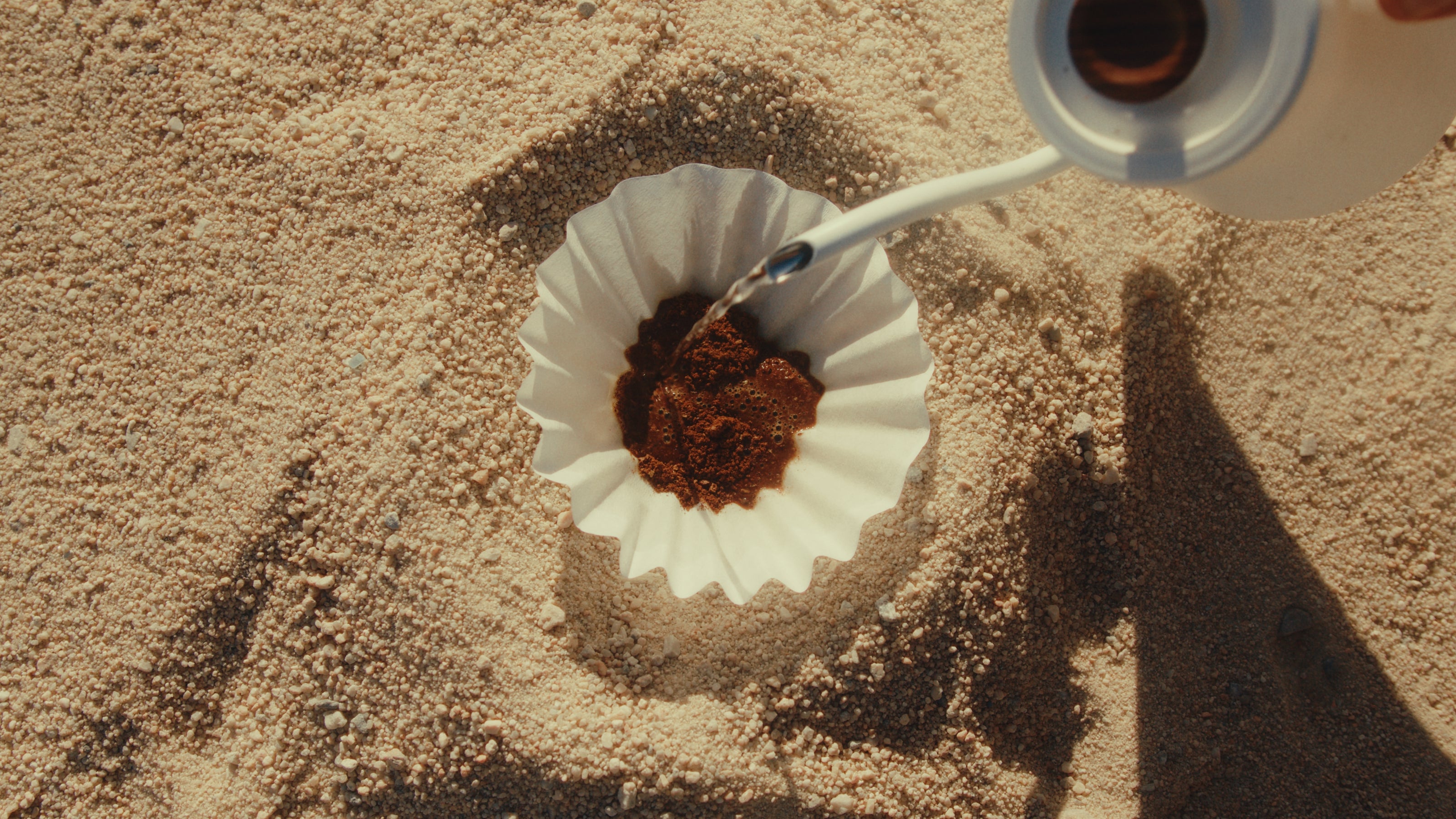 KAFE coffee being poured into a filter on sandy ground