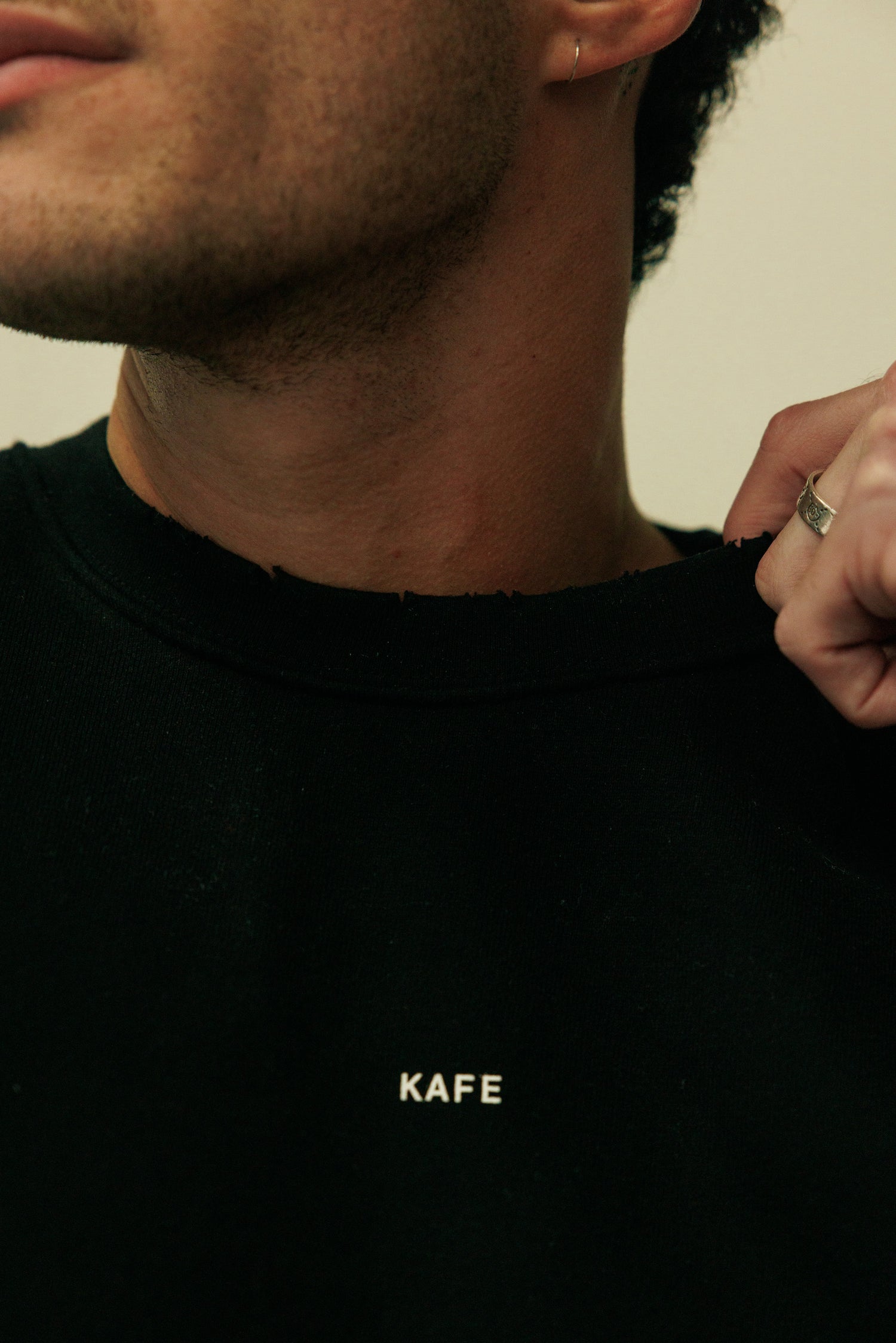Person wearing a black shirt with 'KAFE' logo, close-up of neck and shirt.